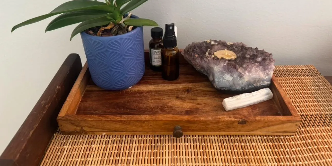 A carved wooden tray in Briana's room holding arnica, massage oil, an amethyst candle holder, a selenite wand, and an orchid
