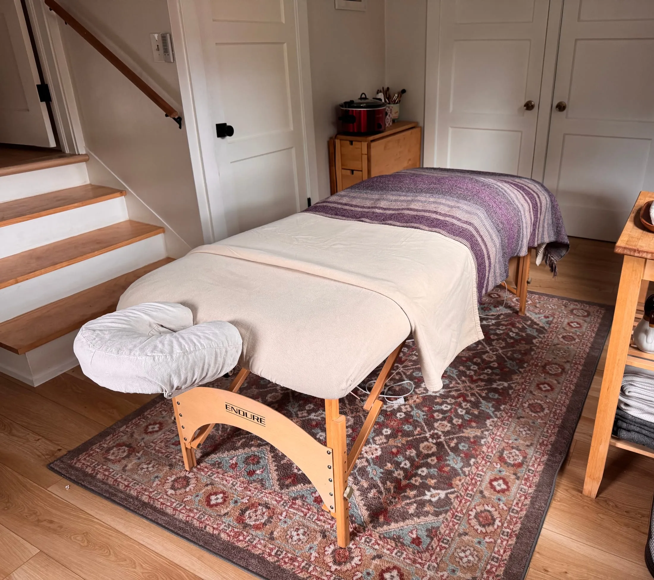 The massage table dressed with linens and a woven blanket in Briana's treatment room